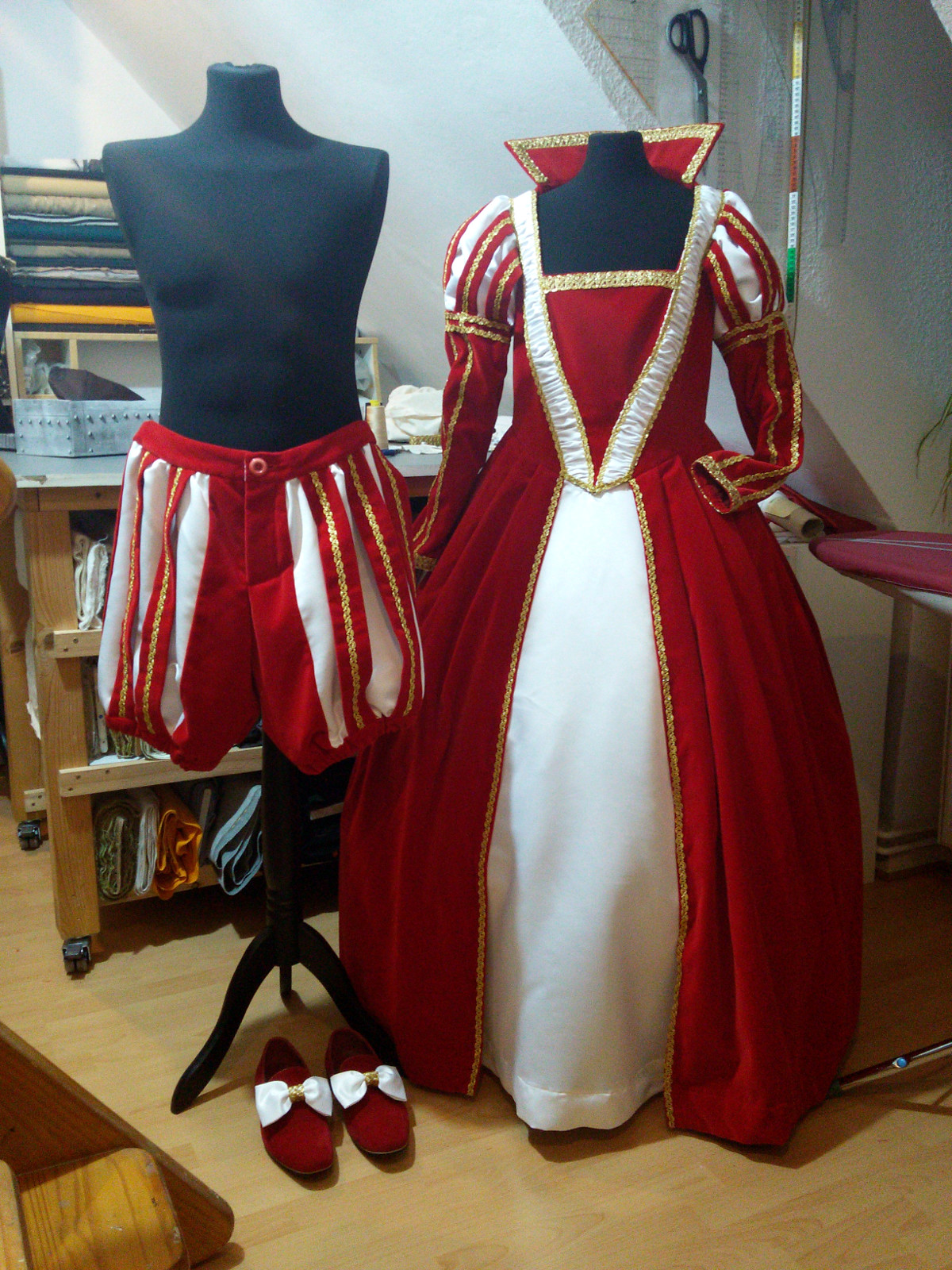 Bild: Hose und Schuhe des Prinzen und Prinzessin-Kleid auf Schneiderpuppen vor einem Tisch mit Stoffballen.